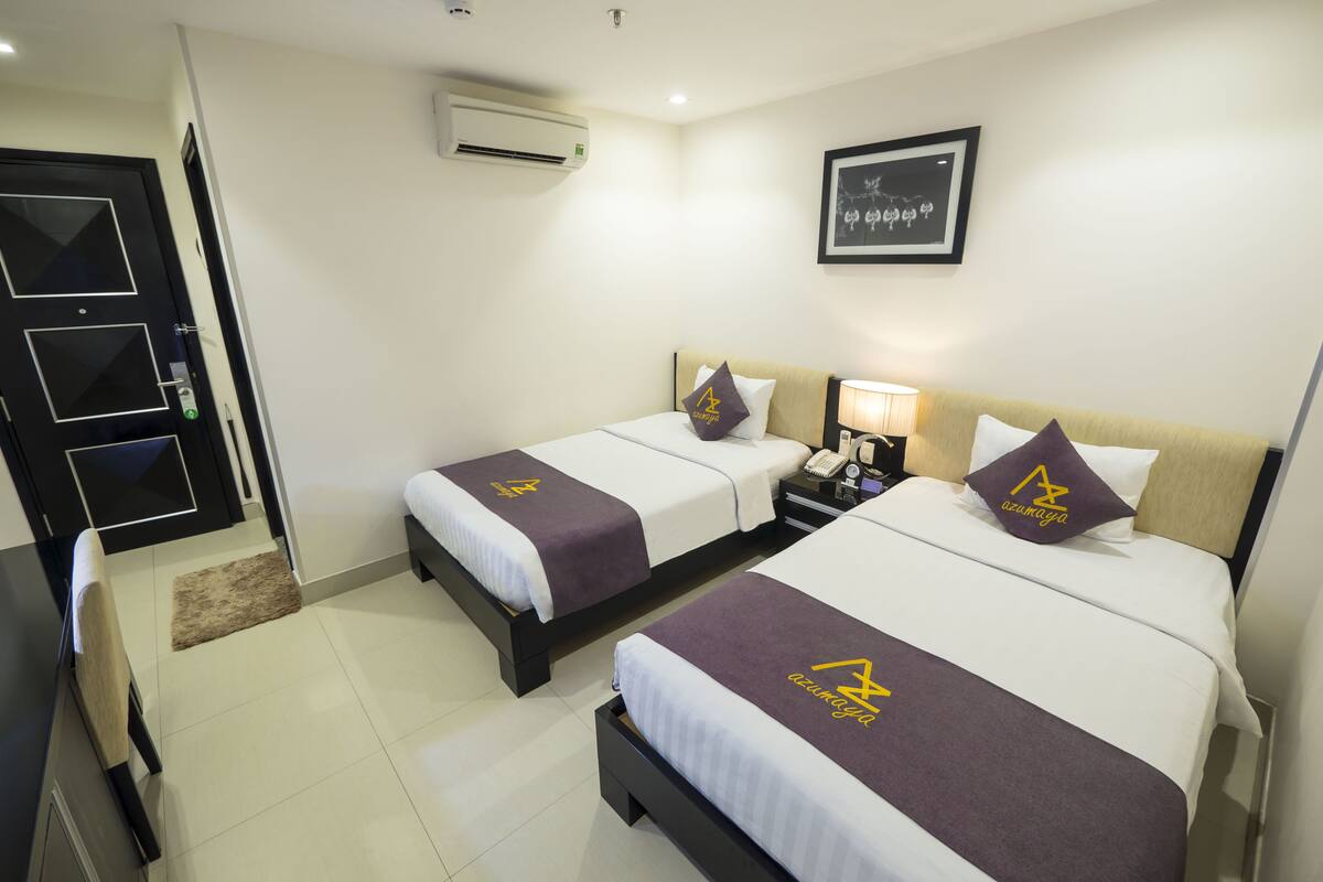 A hotel room with two beds, a nightstand, a lamp, and a framed picture on the wall.