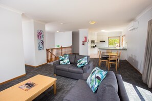 A modern living room with a grey sofa, a wooden coffee table, and a dining area with a wooden table and chairs. - Nightcap at Federal Hotel Toowoomba (East Toowoomba)