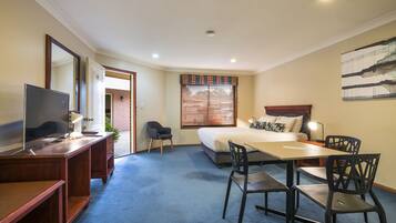 A hotel room with a bed, desk, chairs, a TV, and a window with blinds.