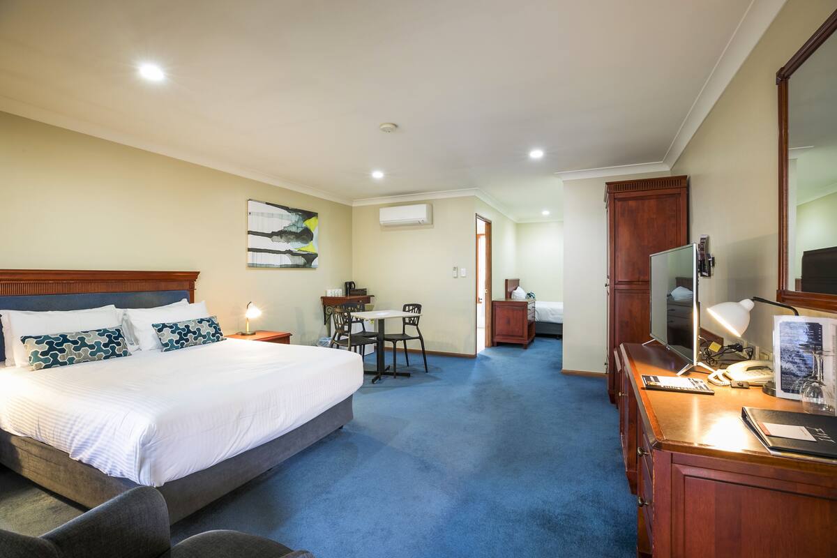 A hotel room with a large bed, a desk with a chair, a desk lamp, a telephone, and a mirror.