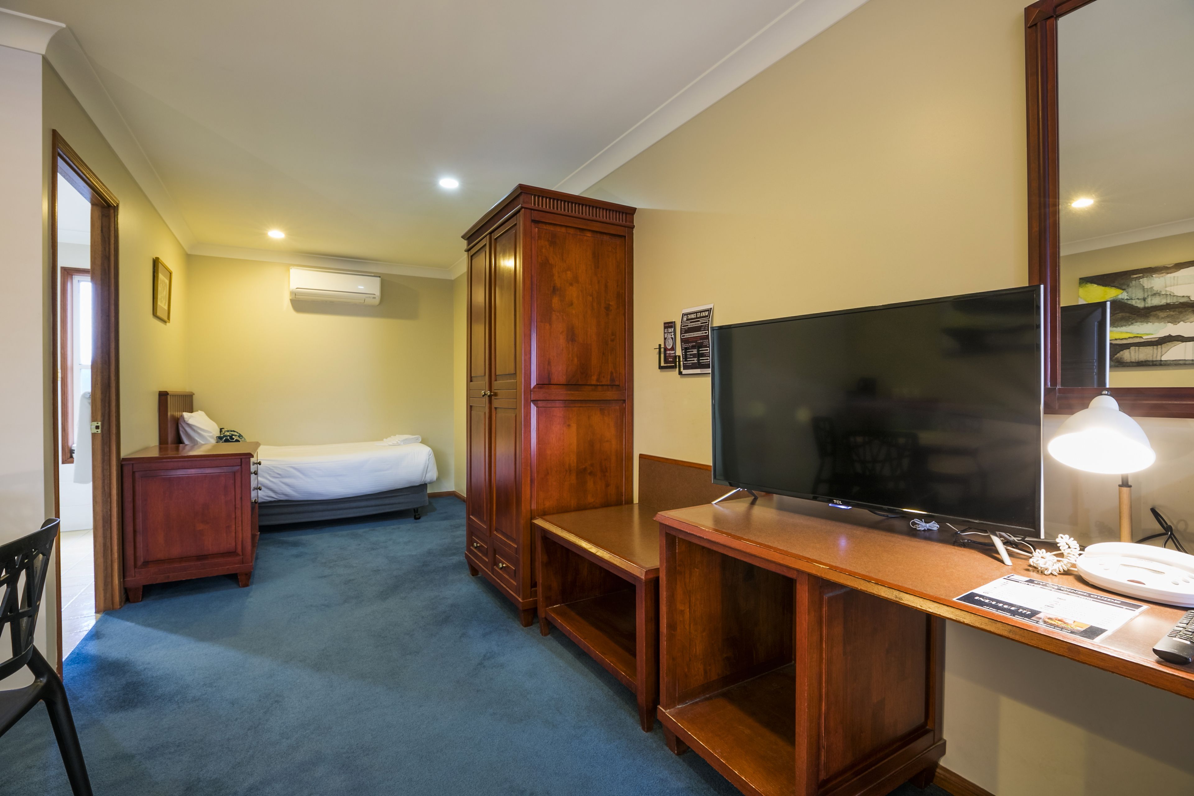 Ein Hotelzimmer mit einem Bett, einem Holzschrank, einem Schreibtisch mit Fernseher und einer Lampe.