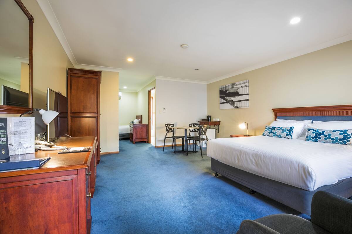 A hotel room with a bed, desk, chair, and a small dining area.