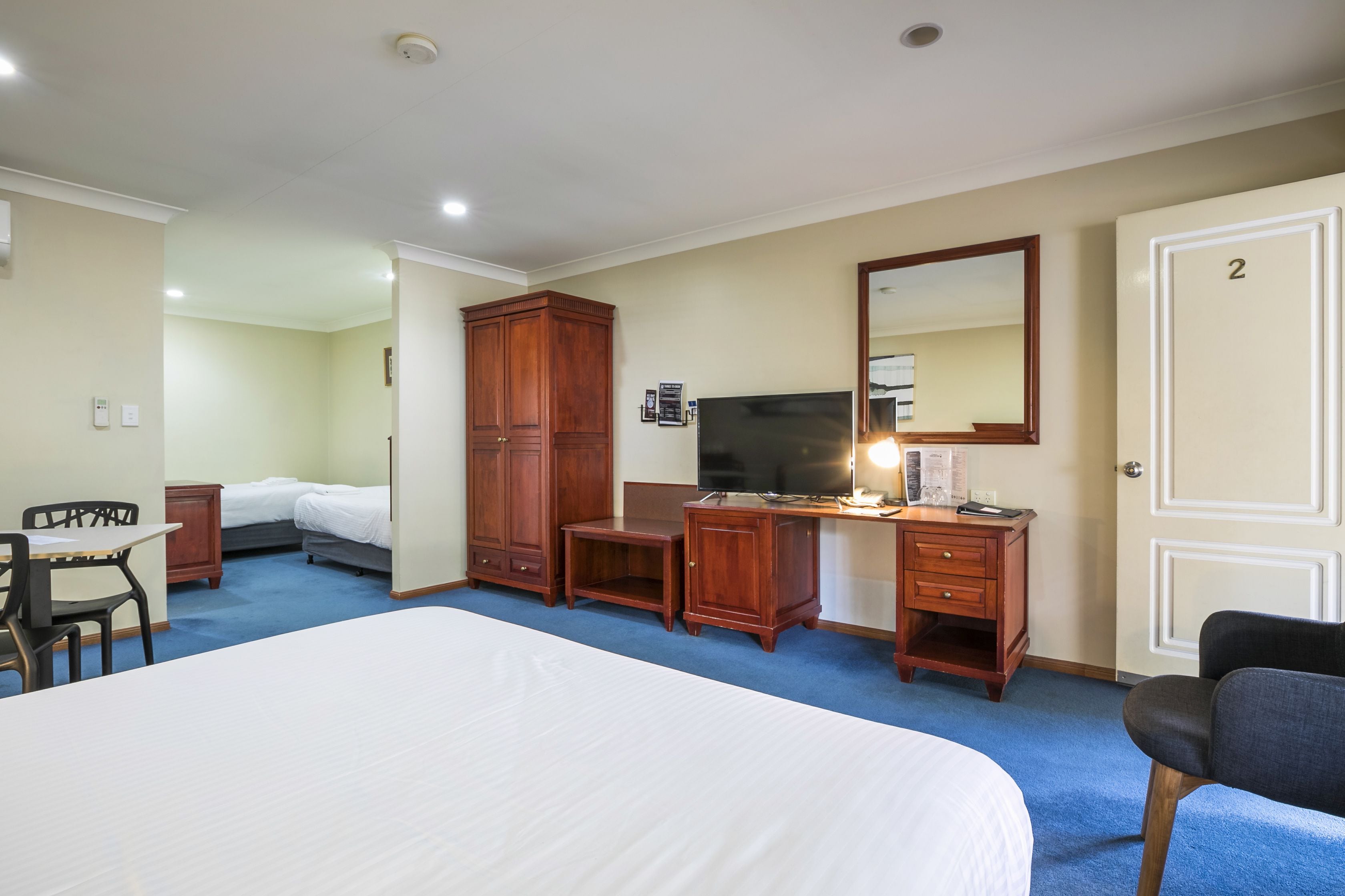 A hotel room with a large bed, a desk with a computer, a TV, and a wardrobe.