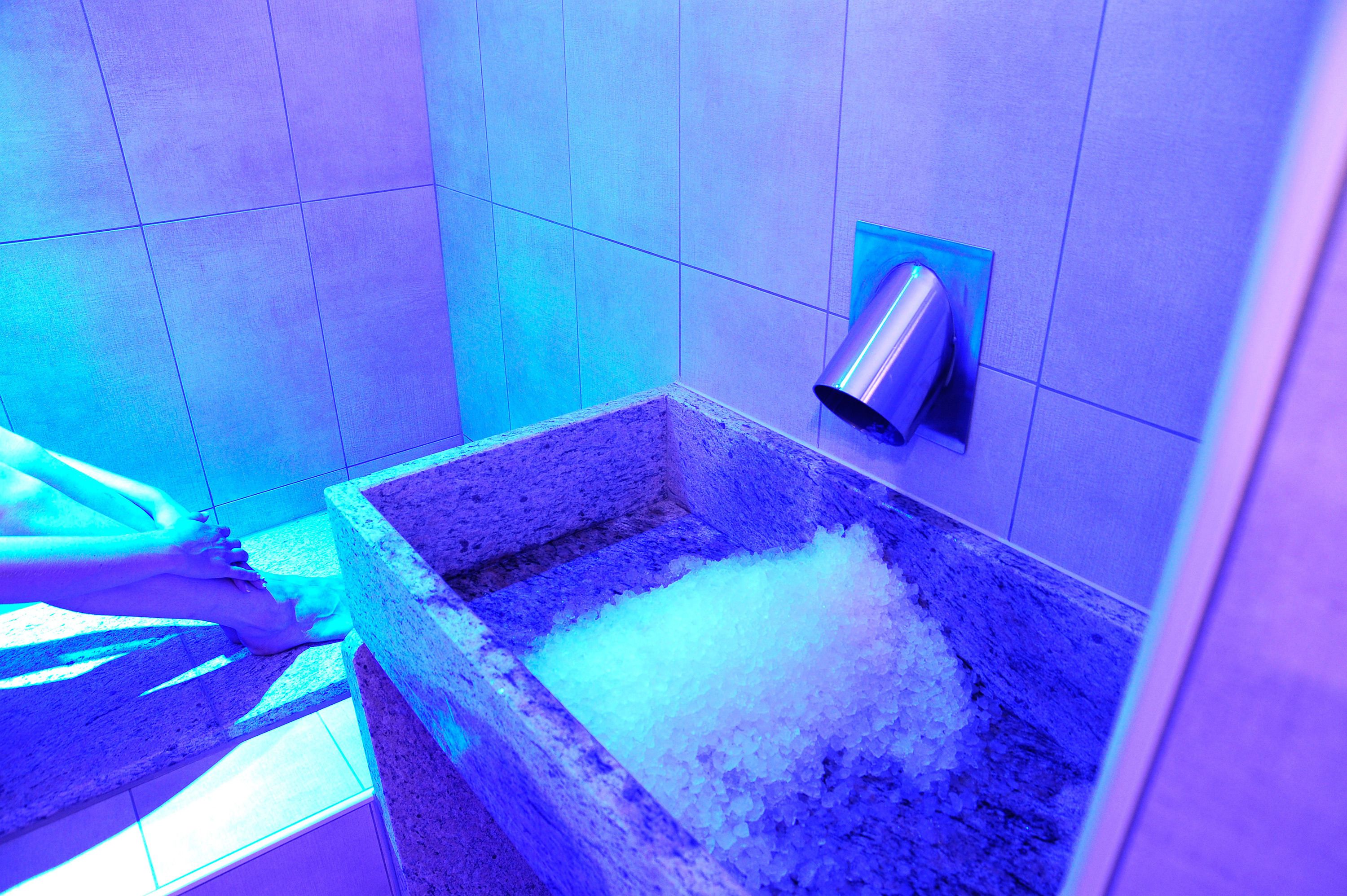 Ein Badezimmer mit einem Becken aus Stein, das mit Eis gefüllt ist, einem an der Wand montierten Fön und einem gefliesten Boden.