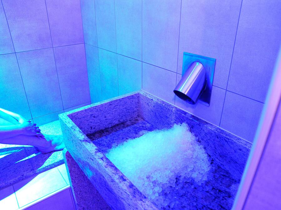 Ein Badezimmer mit einem Becken aus Stein, das mit Eis gefüllt ist, einem an der Wand montierten Fön und einem gefliesten Boden.