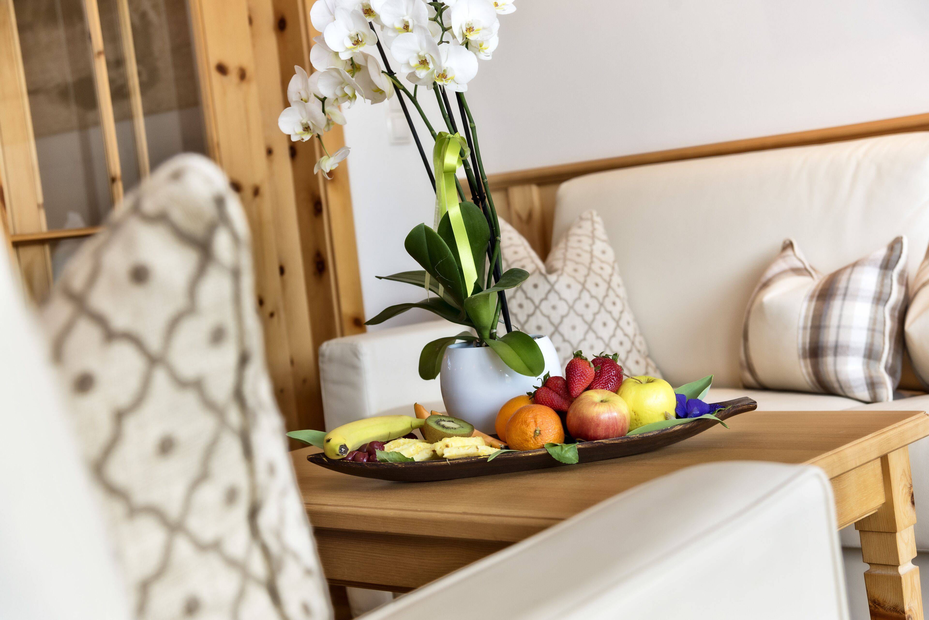 A wooden table with a tray of fruits and a potted orchid.