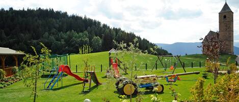 A playground with slides and swings, surrounded by a well-maintained lawn and trees.