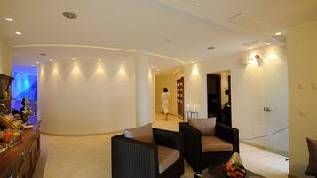 Un'accogliente hall d'hotel moderna con mobili in vimini, un'area reception e una persona con un accappatoio che si dirige verso il fondo.