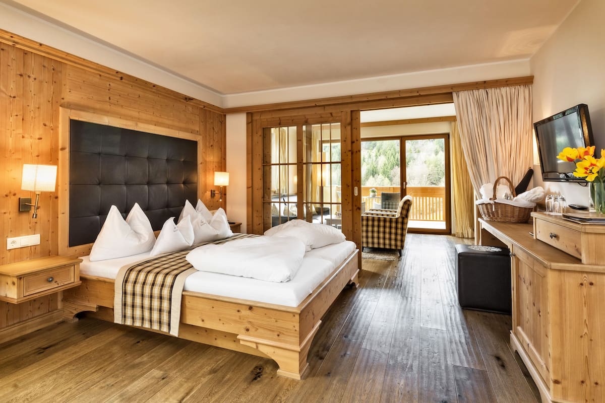 A wooden bedroom with a large bed, bedside tables, a TV, and a balcony with a view.