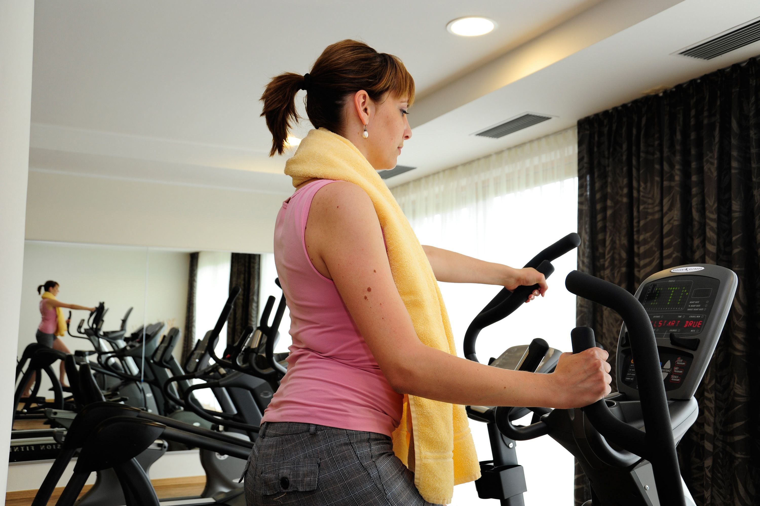 A woman using an exercise bike in a gym with multiple bikes and a mirror on the wall.