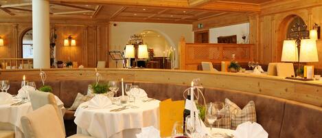 A restaurant with round tables set for dining, featuring white tablecloths and wine glasses.
