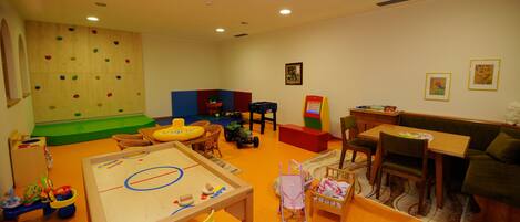 Zona de juegos infantiles con paredes de escalada, una mesa con juguetes y un sofá.