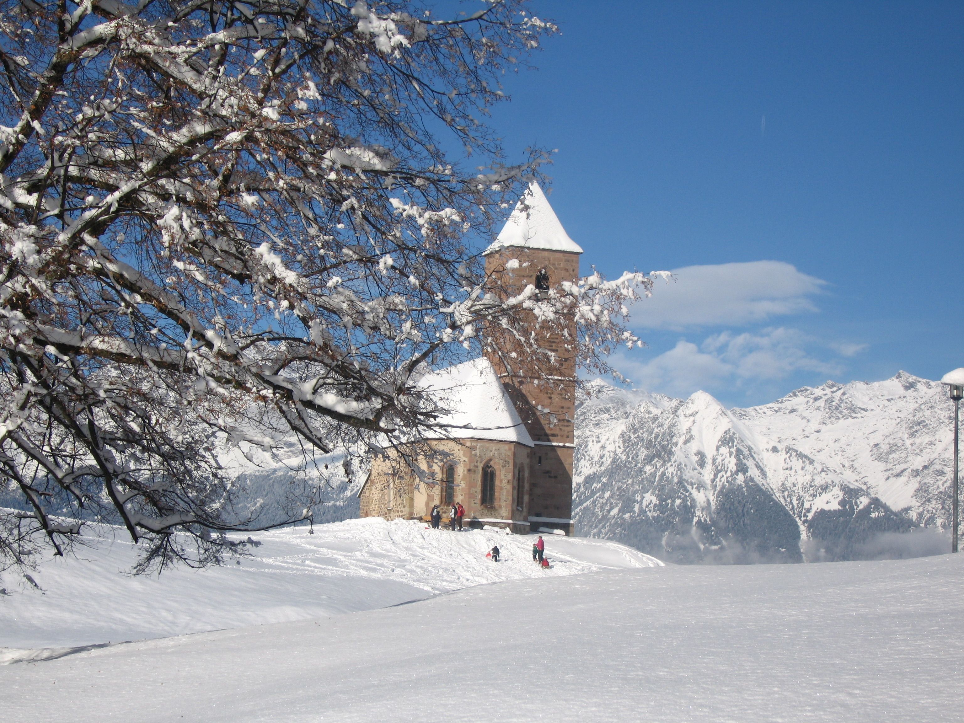 Una iglesia cubierta de nieve con un campanario, rodeada de montañas.