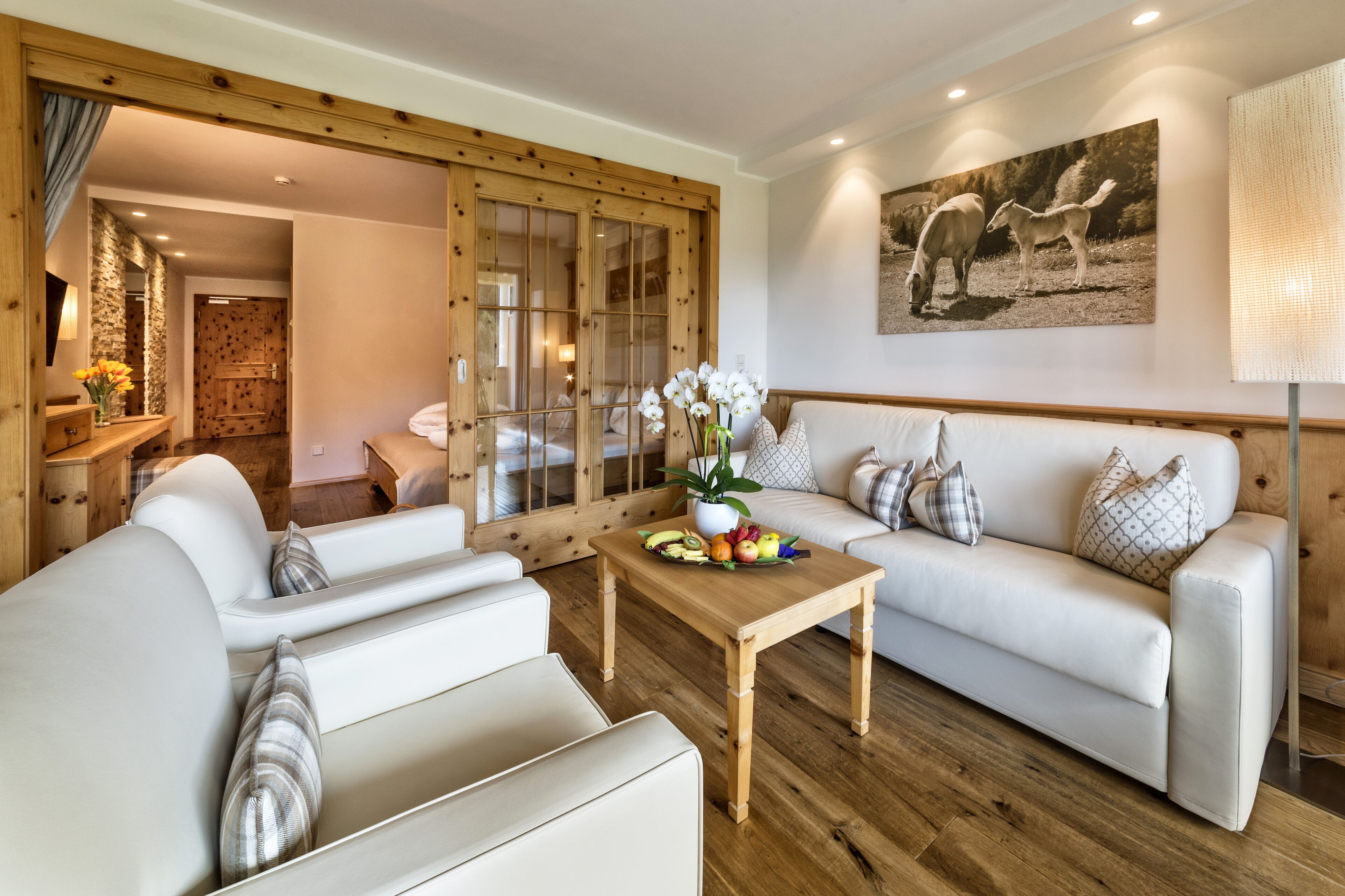 Una sala de estar moderna con piso de madera, sofás blancos, una mesa de centro de madera y un cuadro de caballos en la pared.