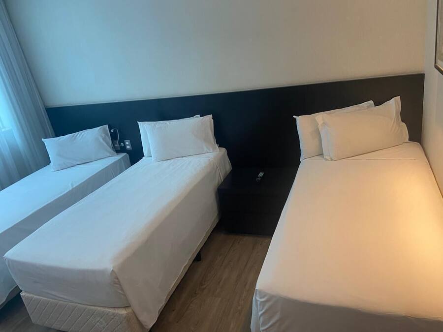 A hotel room with two single beds, a dark headboard, and a window with curtains.