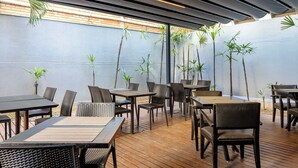 An outdoor dining area with wooden tables and chairs, surrounded by tall plants and a high ceiling with exposed beams. - Hotel Park Tower Savassi (Belo Horizonte)