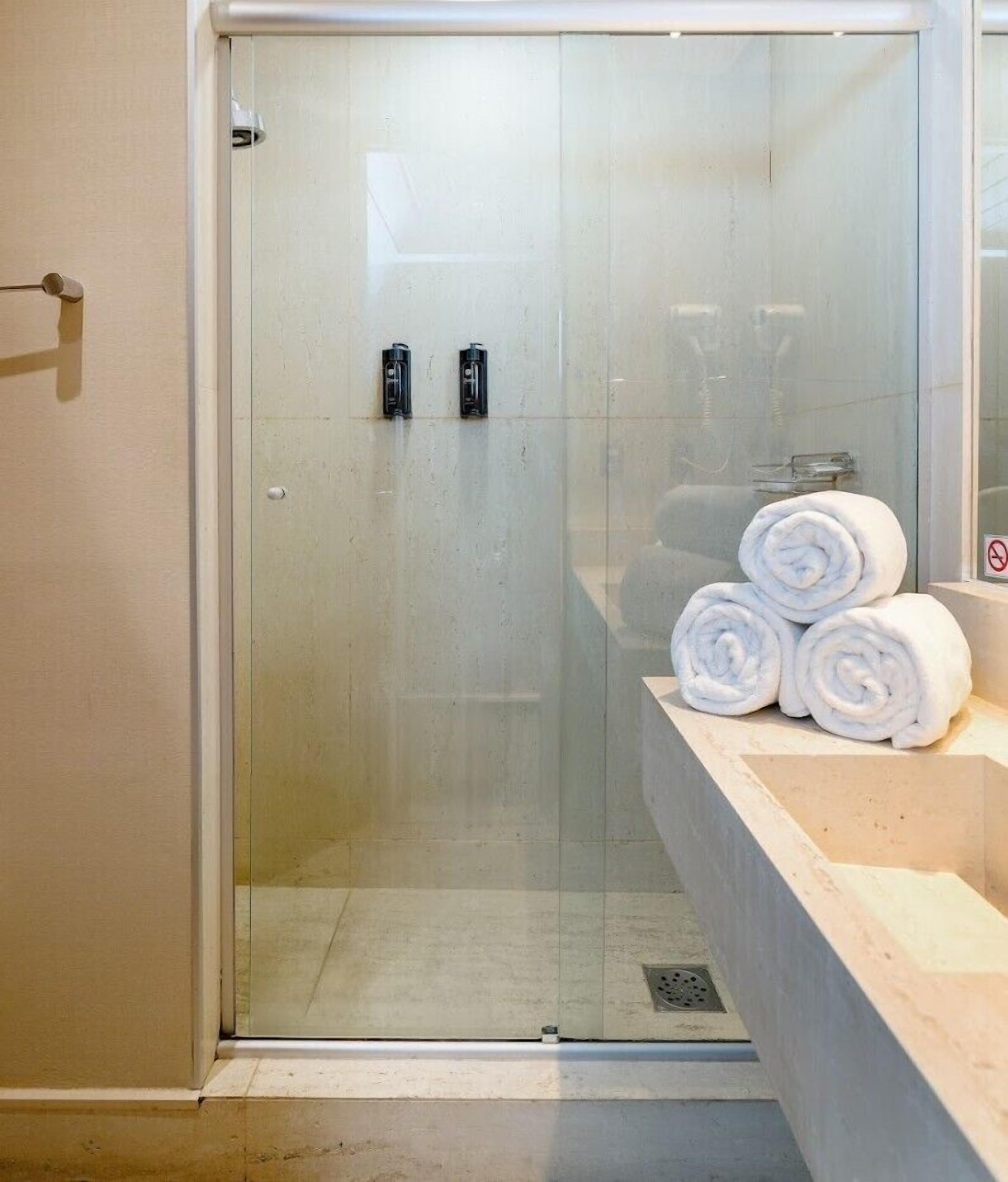 A glass-enclosed shower area with a white sink and rolled towels on the counter.