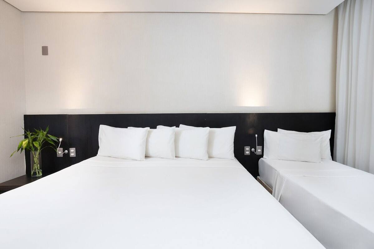 Habitación de hotel moderna con una cama grande, cabecera negra y una mesita de noche con lámpara.