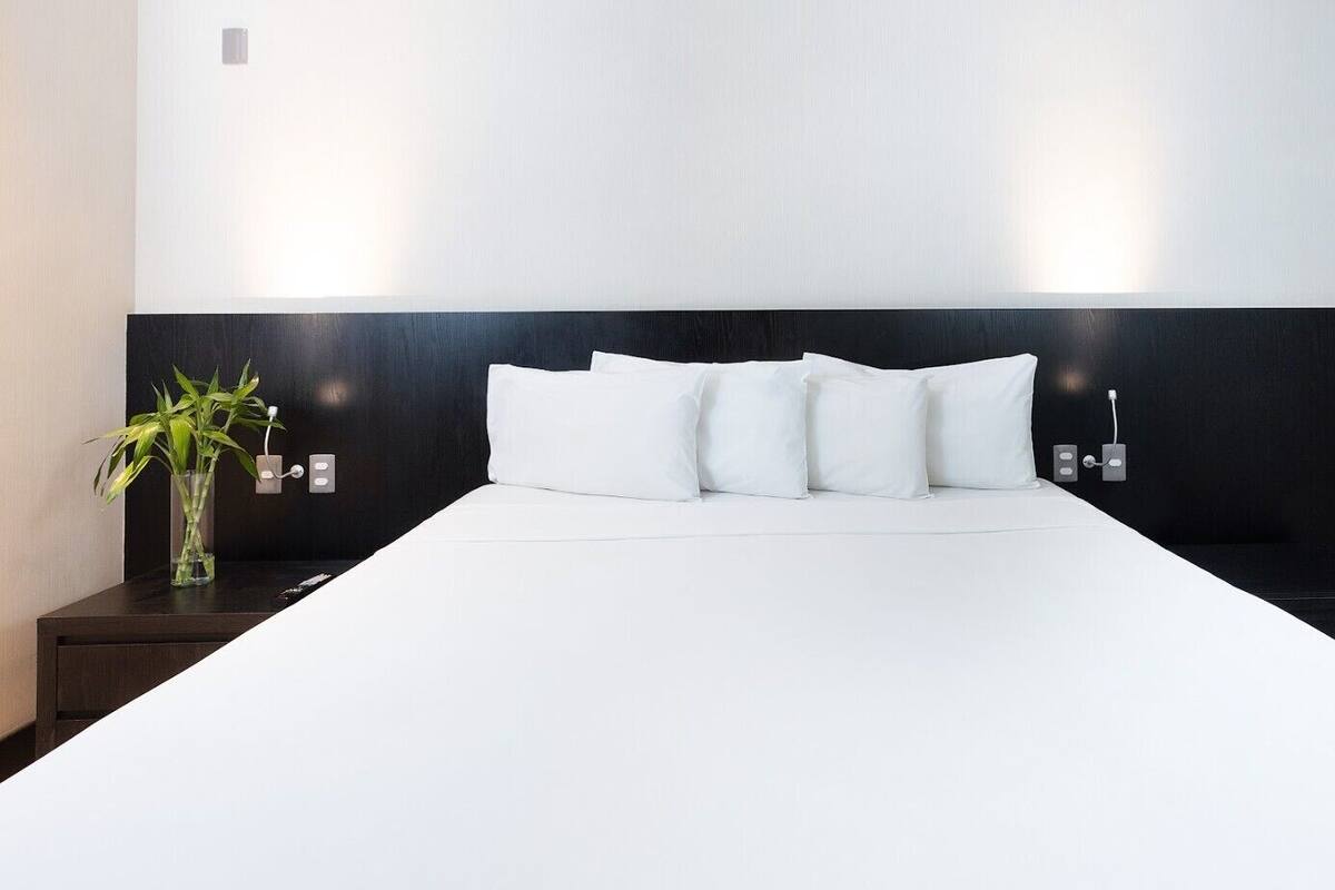 Una habitación de hotel con una cama grande, una mesita de noche con una planta y una mesita con una lámpara.