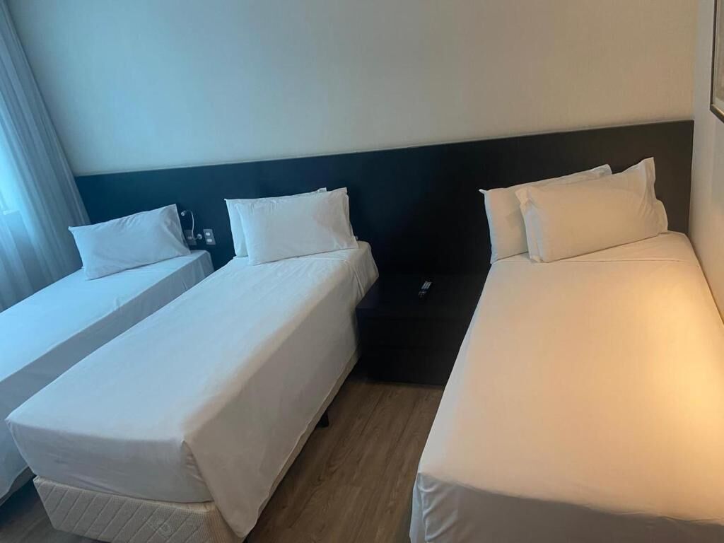 Ein Hotelzimmer mit zwei Einzelbetten, einem dunklen Kopfteil und einem Nachttisch.