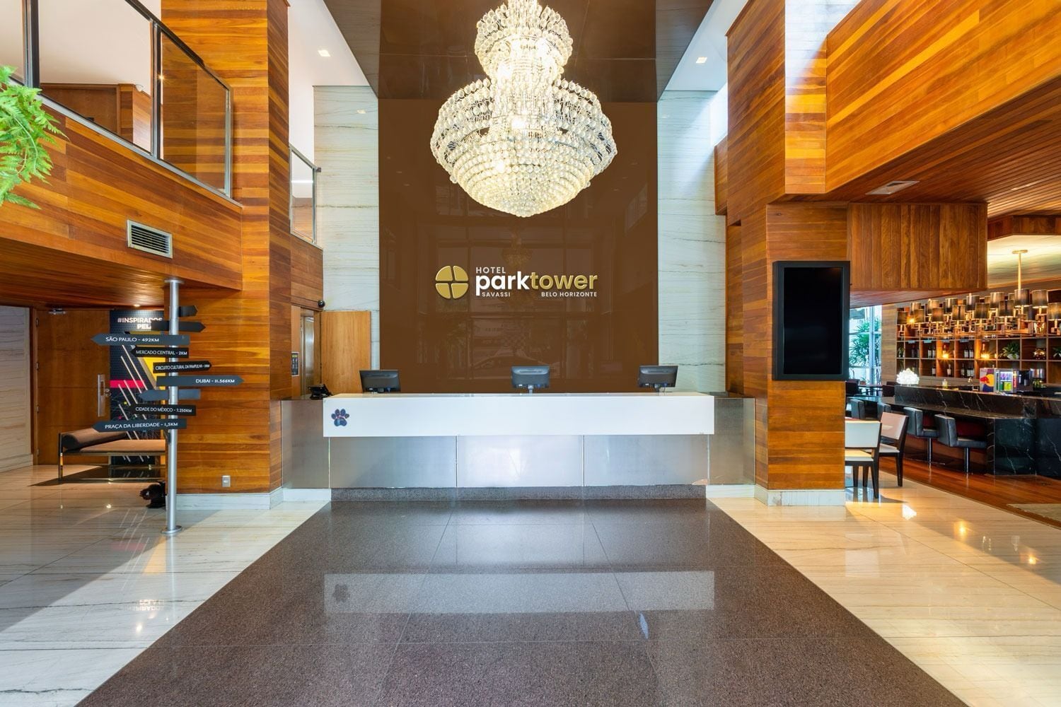 A hotel reception area with a chandelier, a reception desk, and a bar area.