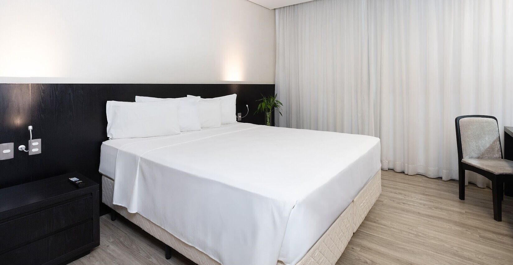 Una habitación de hotel con una cama grande, una mesita de noche, una silla y una ventana con cortinas.