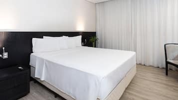 Una habitación de hotel con una cama grande, una mesita de noche, una silla y una ventana con cortinas.