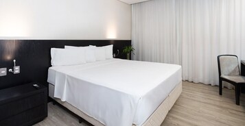 Una habitación de hotel con una cama grande, una mesita de noche, una silla y una ventana con cortinas.