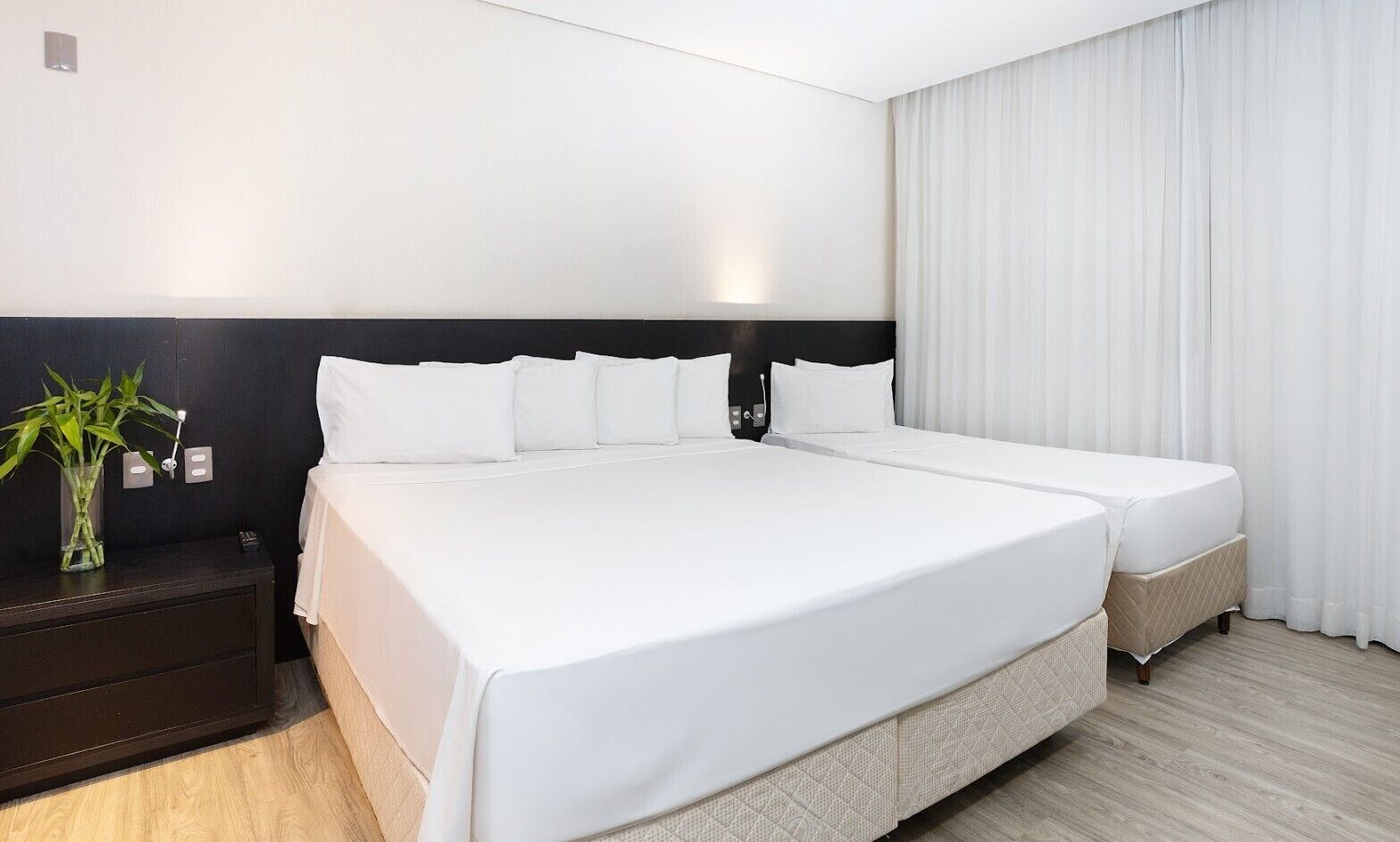 A large bed with white bedding, a dark headboard, and a bedside table with a plant.