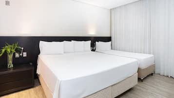 A large bed with white bedding, a dark headboard, and a bedside table with a plant.