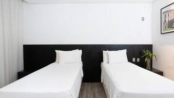 A hotel room with two single beds, a black headboard, a small bedside table with a vase of plants, and a framed picture on the wall.