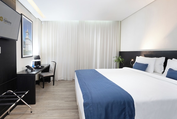 Une chambre d’hôtel avec un grand lit, un bureau avec une chaise, un ordinateur portable et une plante.