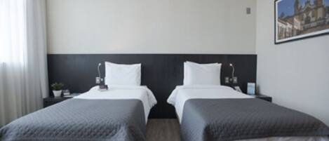A hotel room with two beds, a nightstand with a lamp, a small table with a plant, and a framed picture on the wall.