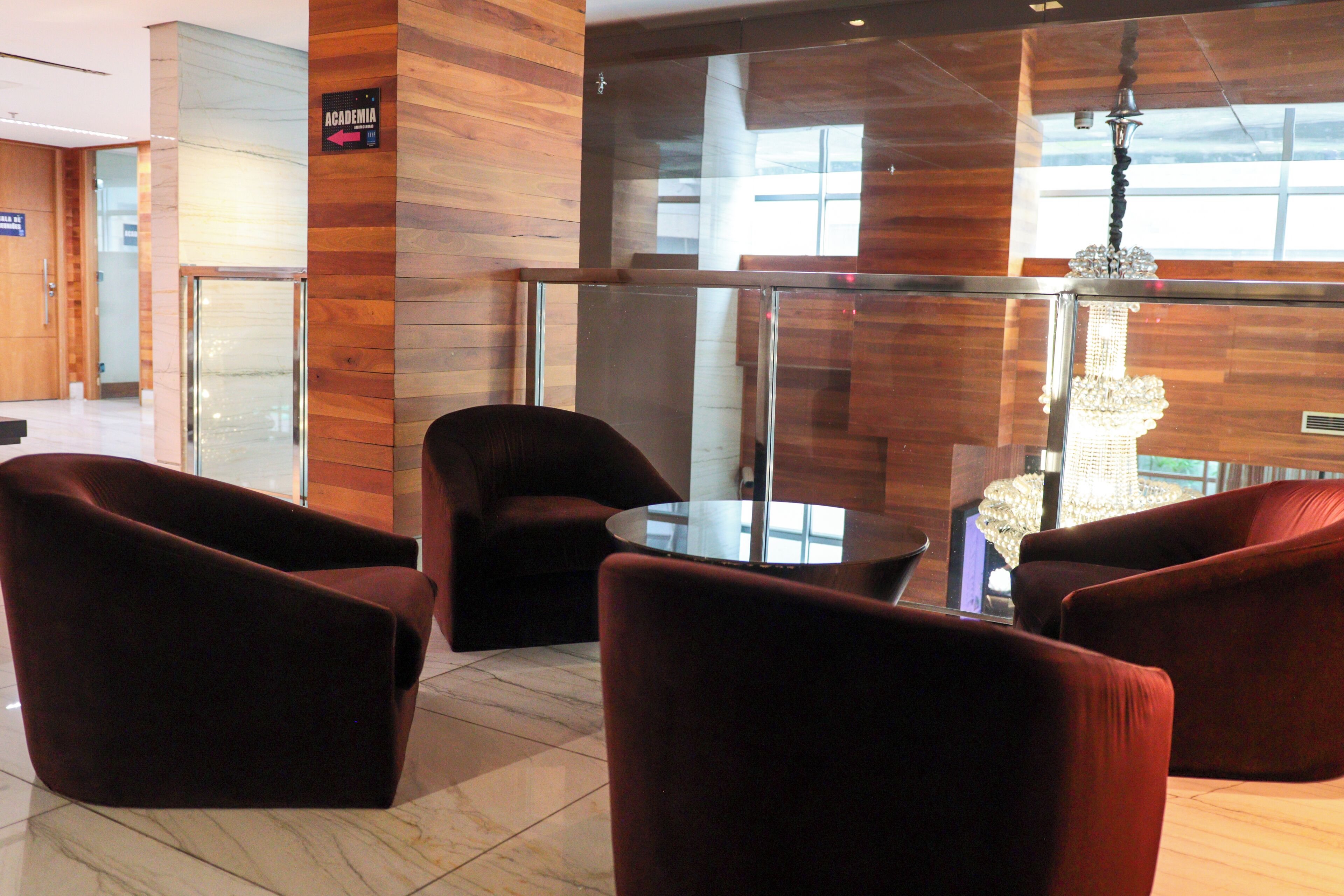 A lobby with wooden paneling, a glass elevator, and a chandelier.