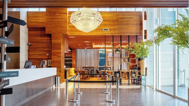 A hotel lobby with a reception desk, a chandelier, a seating area, and a large window. - Hotel Park Tower Savassi (Belo Horizonte)
