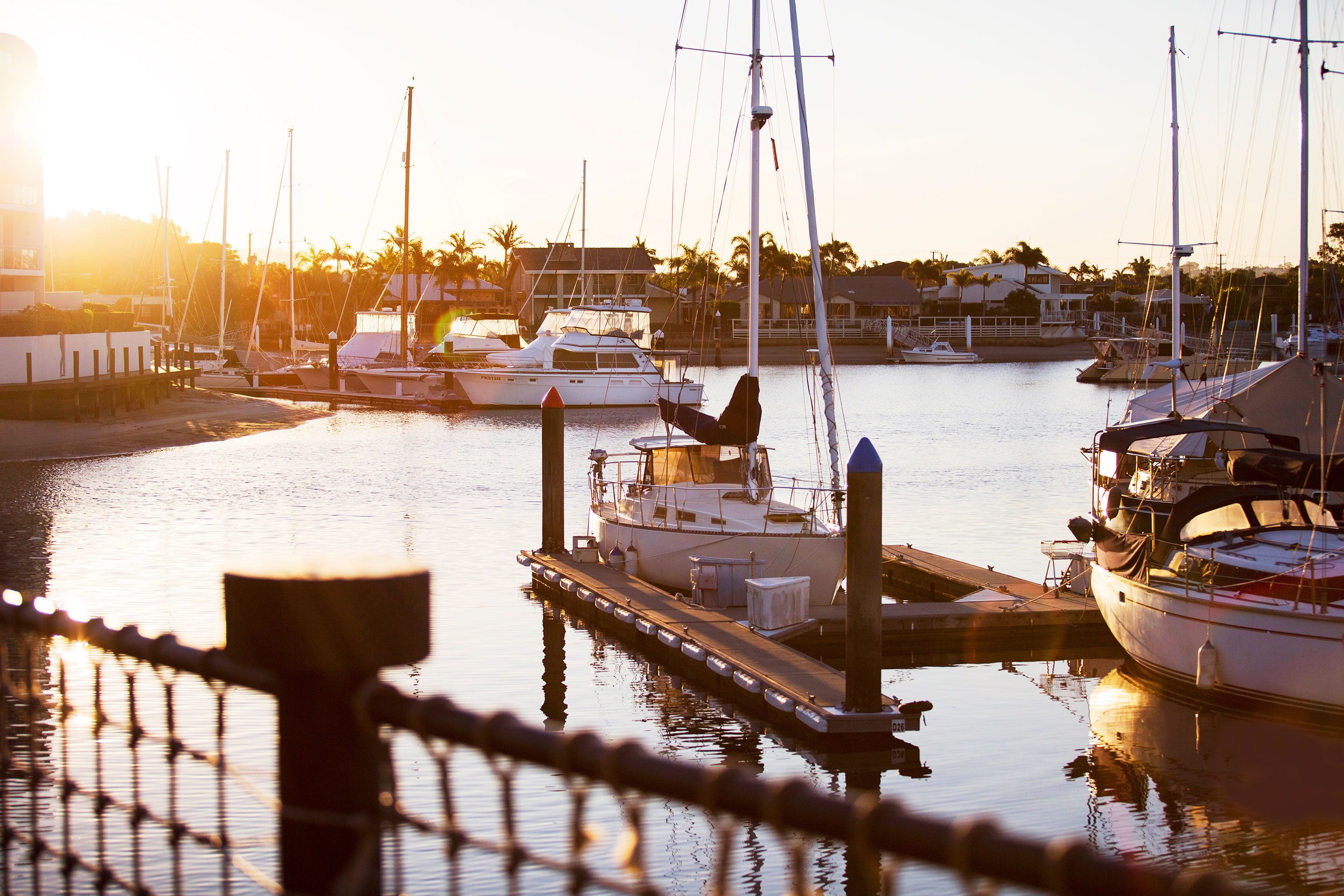 A marina with boats docked at wooden piers, surrounded by buildings and palm trees.