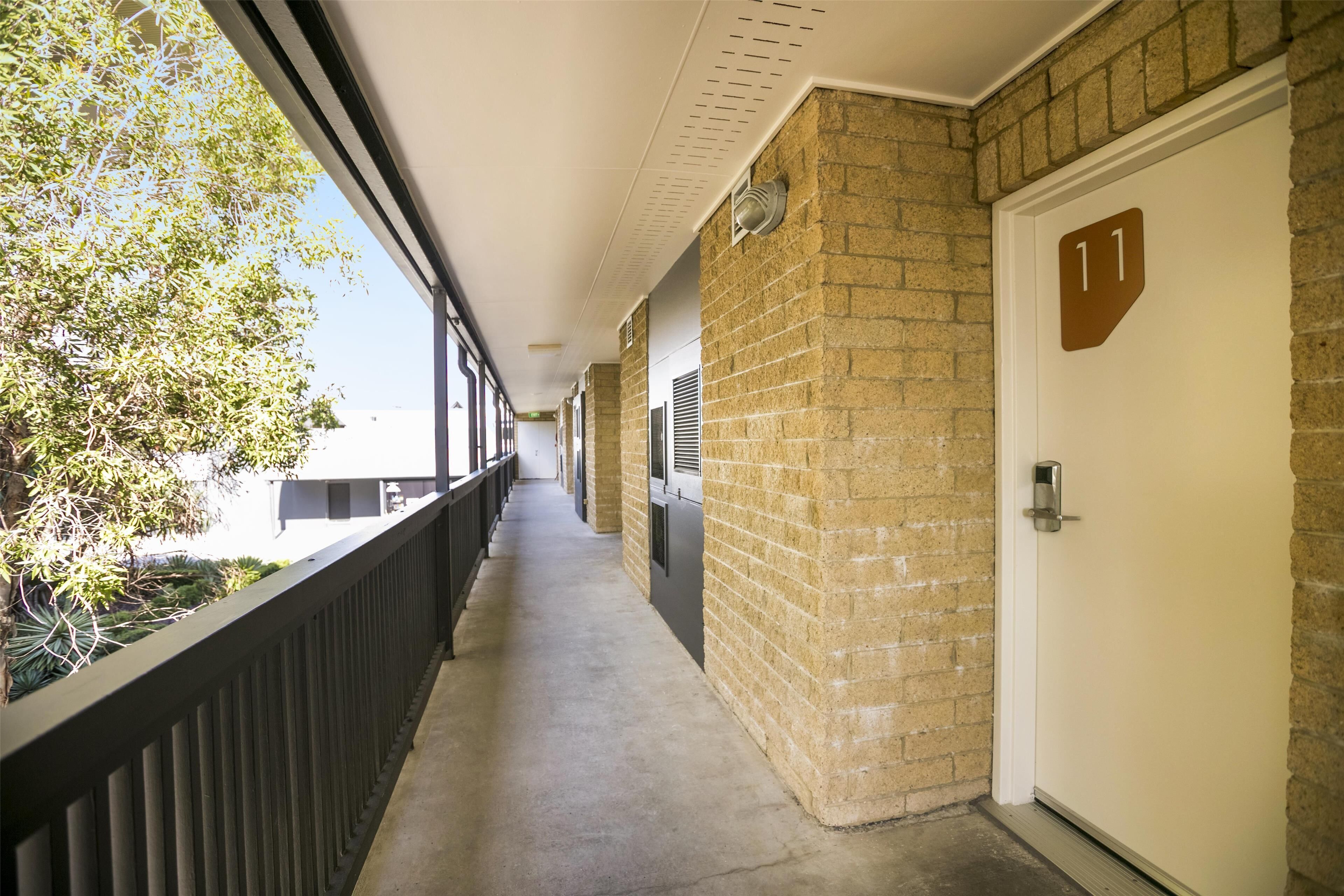 A corridor with a brick wall, a door marked with the number 11, and a window on the left.