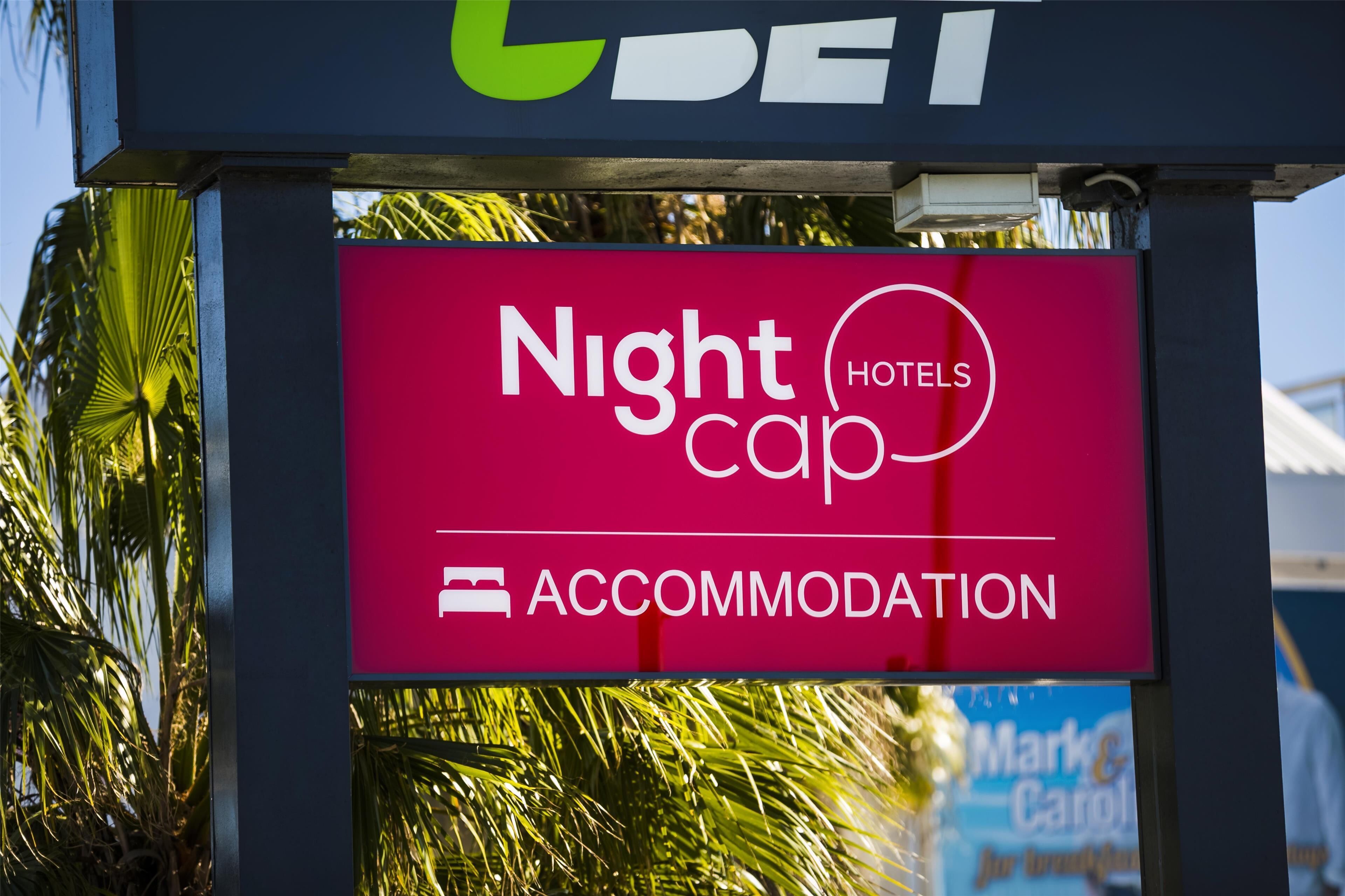 A sign for Nightcap Hotels with a clear view of palm trees in the background.