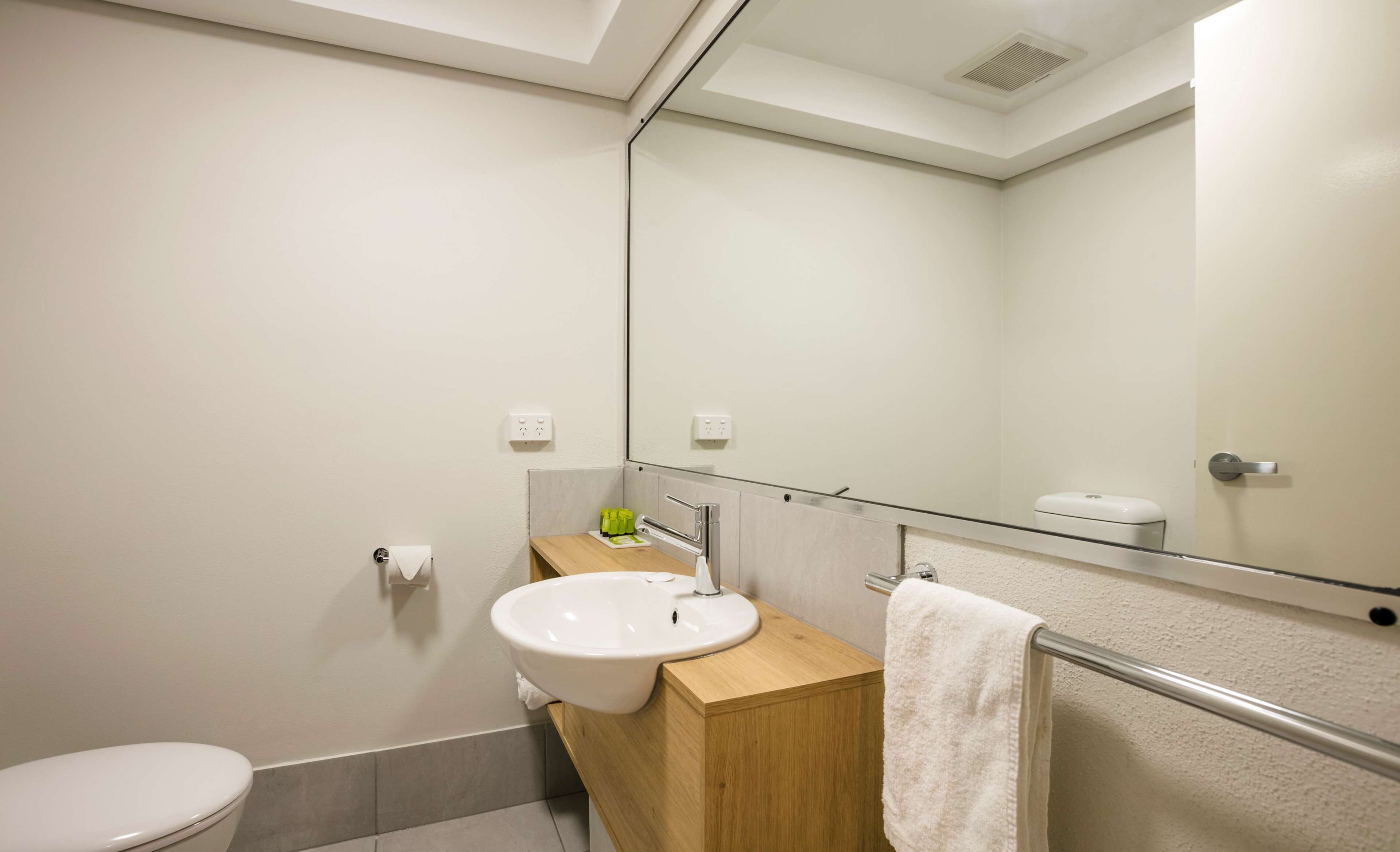 A modern bathroom with a white toilet, a wooden vanity with a white sink, and a glass shower enclosure.