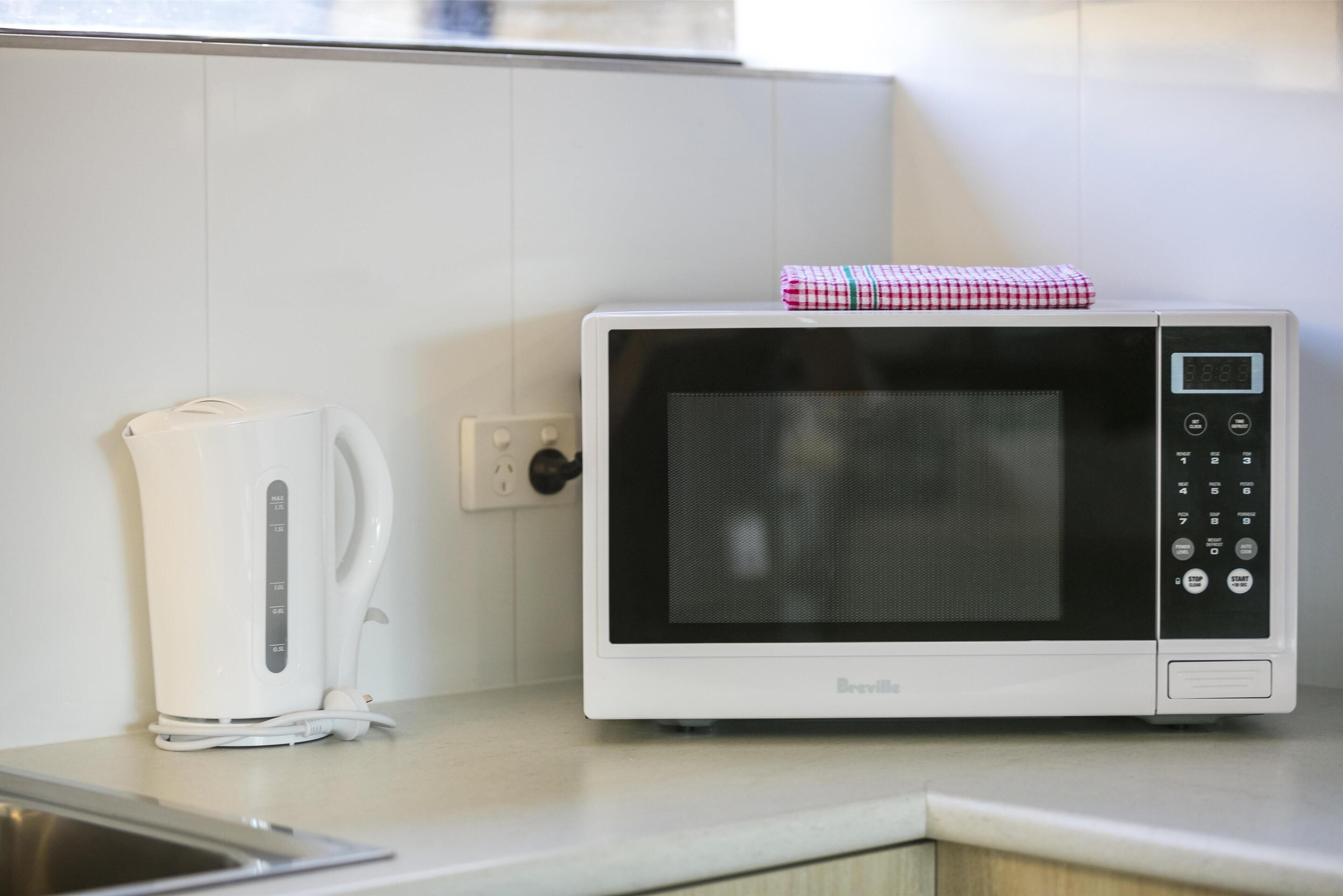 Une cuisine avec un four à micro-ondes blanc, une bouilloire blanche et un évier en acier inoxydable.