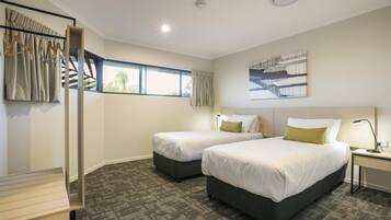 A hotel room with two beds, a desk, a chair, a window with curtains, a ceiling light, and a painting on the wall.