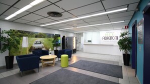 A modern hostel lobby with a reception desk, seating area, and a large welcome sign. - Forenom Hostel Vantaa Airport (Vantaa)