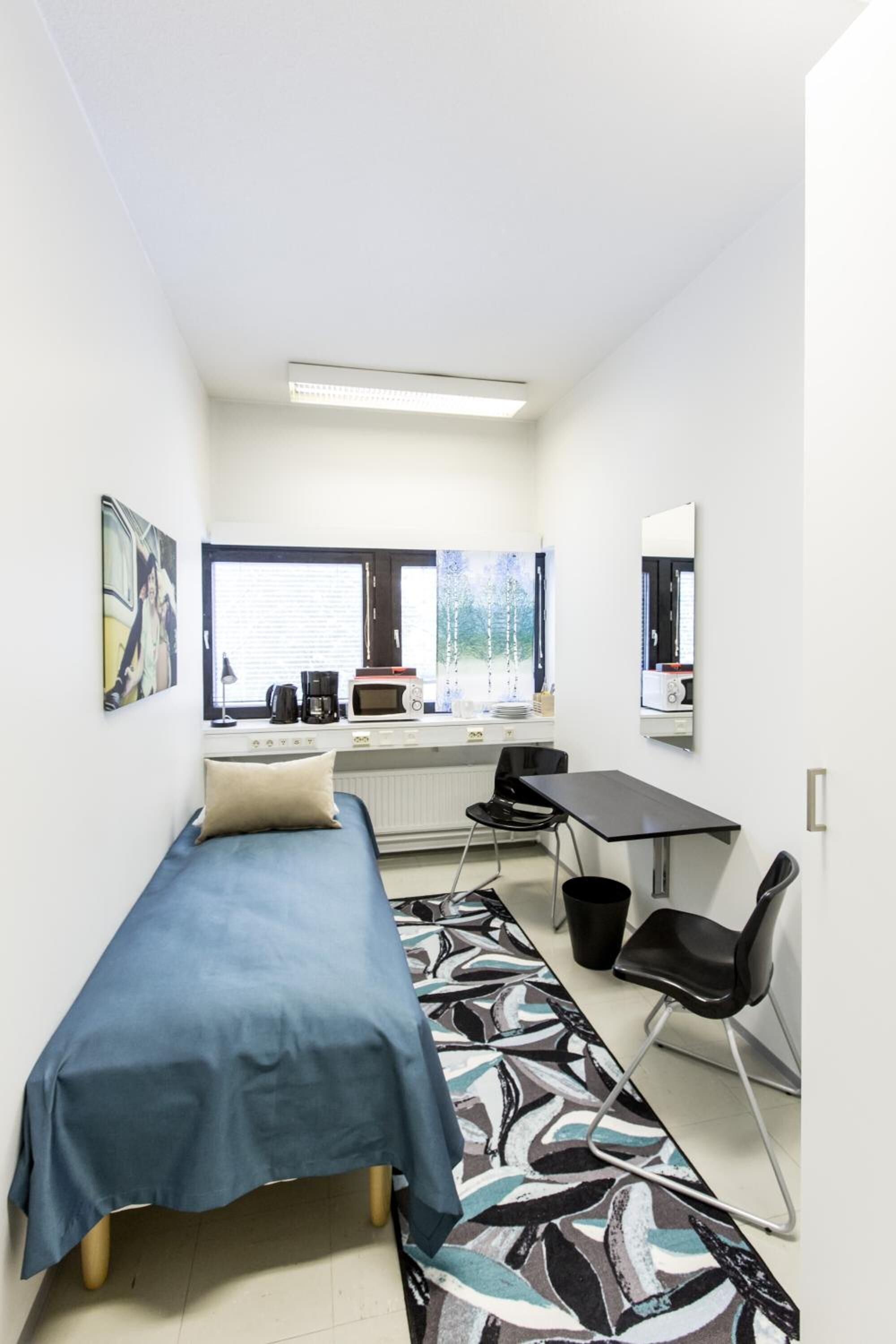 Una habitación pequeña con cama, escritorio, silla, radiador y ventana con persianas.