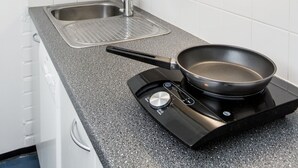 A kitchen with white cabinets, a stainless steel sink, a black induction cooktop, and a frying pan. - Forenom Hostel Vantaa Airport (Vantaa)