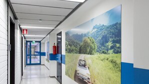 A corridor with a blue and white color scheme, a fire extinguisher, and a door with an exit sign. - Forenom Hostel Vantaa Airport (Vantaa)