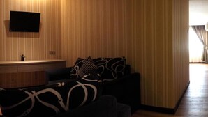 A modern living room with a sofa, a flat-screen TV mounted on the wall, and a wooden panel wall. - Mandarin Hotel (Kota Kinabalu)