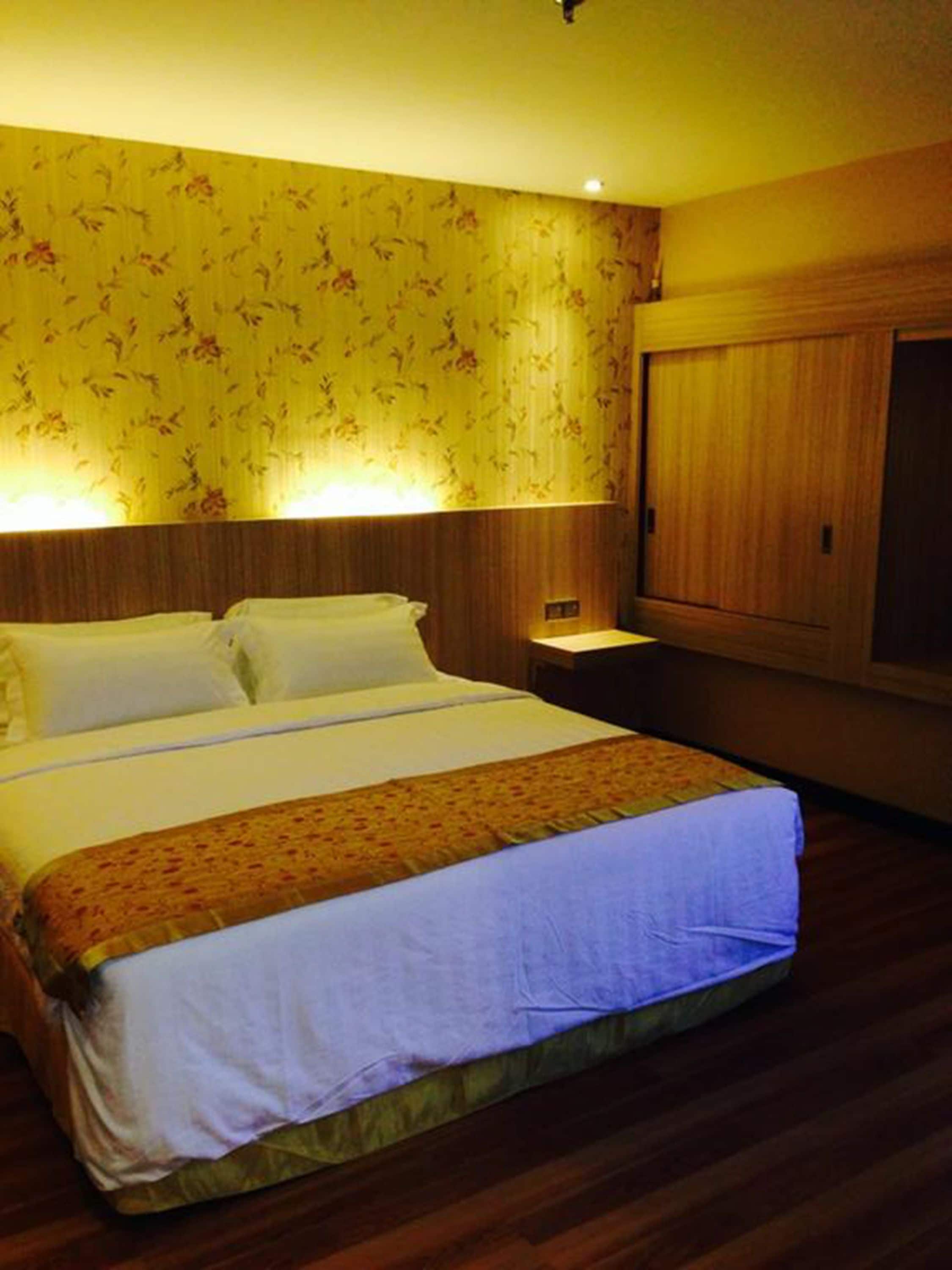 A hotel room with a large bed, wooden headboard, floral wallpaper, and a wooden wardrobe.