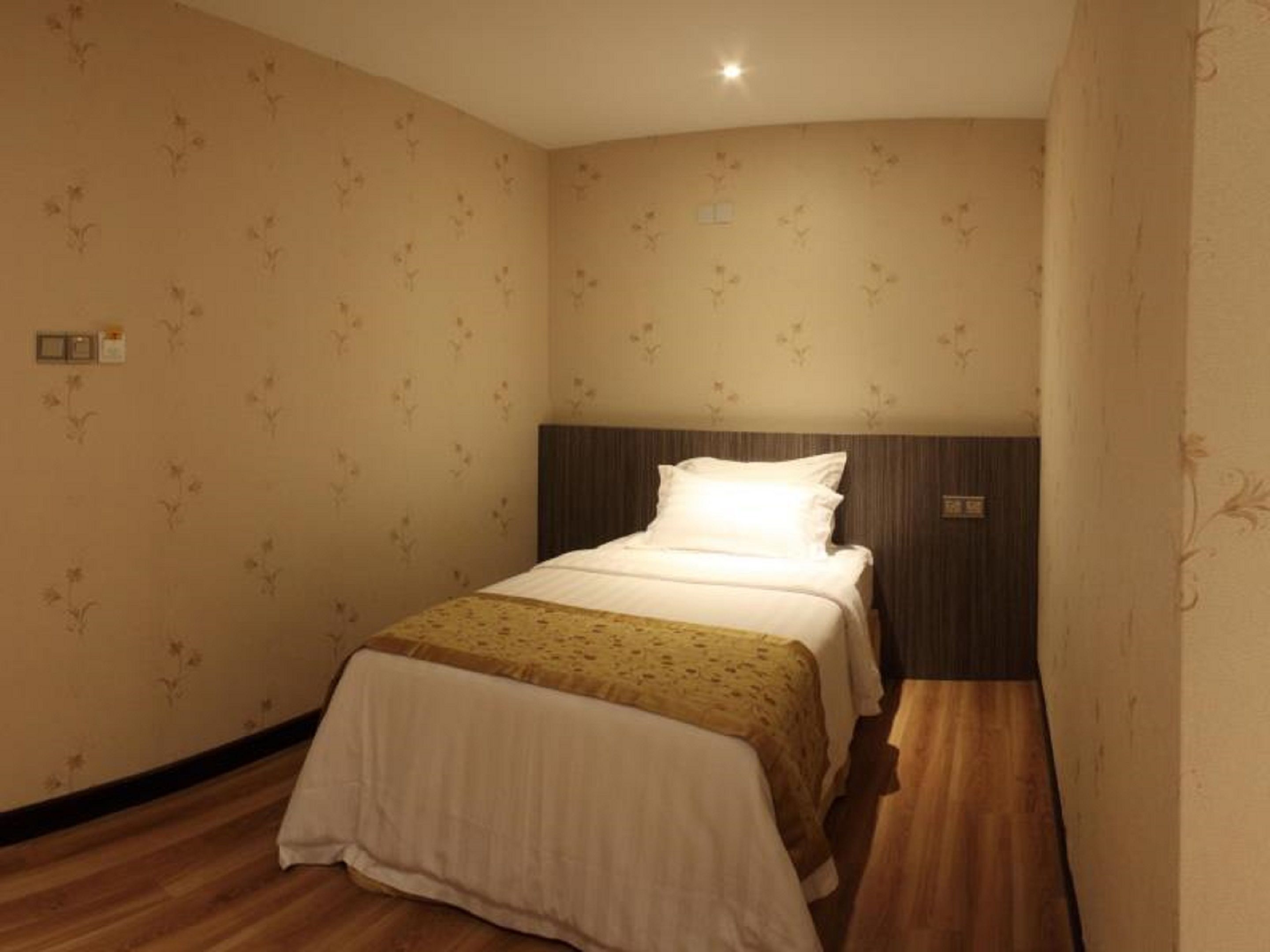 Een kleine, verzorgde slaapkamer met een enkel bed, bloemenbehang en houten vloeren.