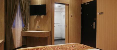 A hotel room with a bed, a desk, a TV, and a door leading to a shower area.