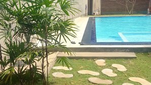 A swimming pool with a stone pathway leading to it, surrounded by grass and plants. - Ocean View Guesthouse (Negombo)
